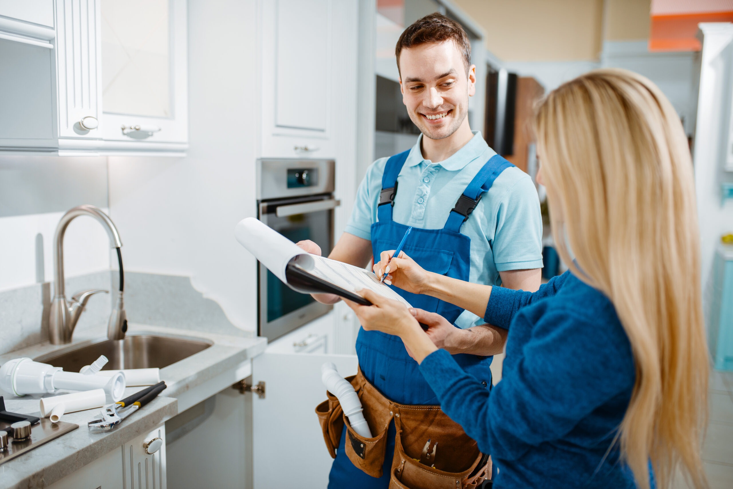 A cheerful contractor discusses plumbing plans with a client in a modern kitchen, highlighting collaboration on home improvements.